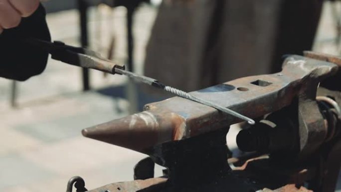 铁匠用锤子和钳子用铁水制成刀柄。铁匠铺在铁砧上击败铁锤。在街上锻造。特写。铁水，铁。
