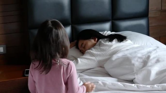 可爱的亚洲小女孩早上躺在家里的床上叫醒妈妈。