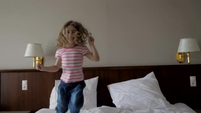 快乐的孩子小女孩跳到床上，快乐的家庭概念慢动作。4K UHD。玩得开心的女孩在卧室跳床玩耍。