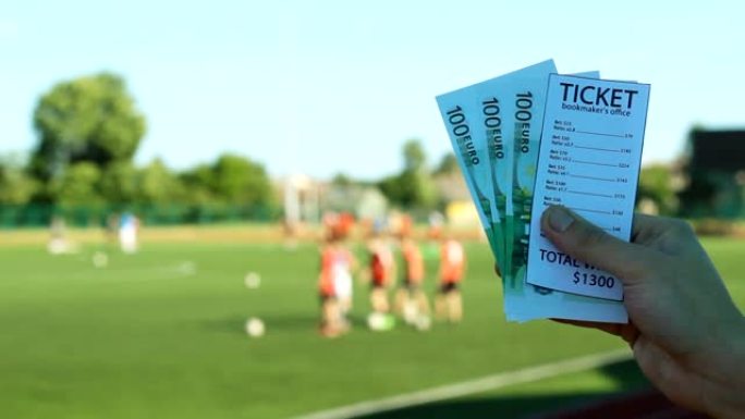 在一场体育场足球比赛的背景下，一名男子拿着庄家的彩票和欧元钞票