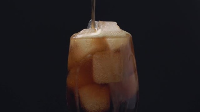 将可乐和冰块倒入黑色背景的玻璃中。