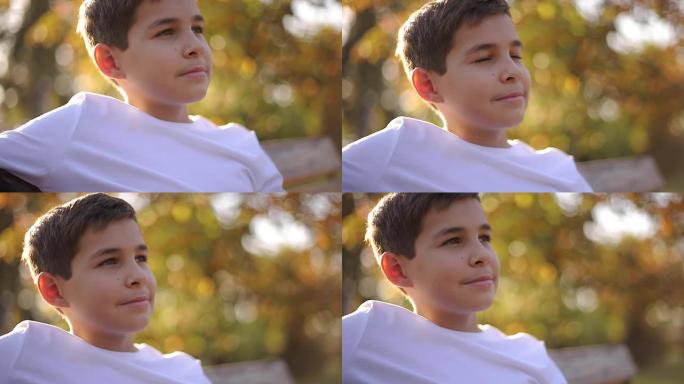 坐在长凳上的穿着白色毛衣的十几岁男孩的特写镜头。秋季公园里有背包的帅气男生