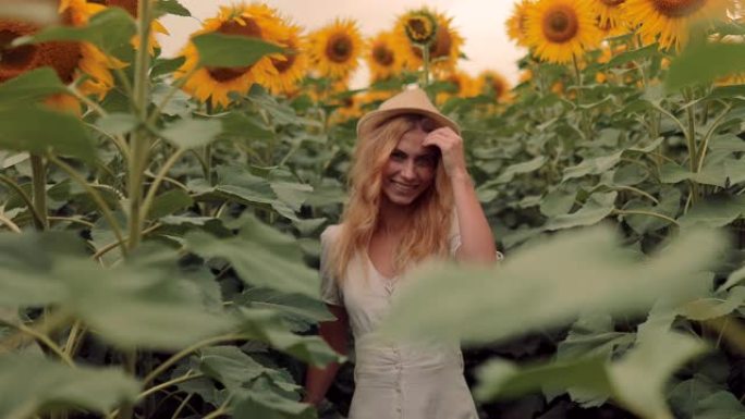 戴着帽子的漂亮女孩在向日葵的田野里旋转。年轻的女人在向日葵上转身微笑。