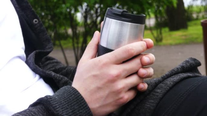户外喝茶或咖啡时间。年轻人在公园里拿着保温杯/马克杯/罐子茶或咖啡。主题旅行或娱乐。