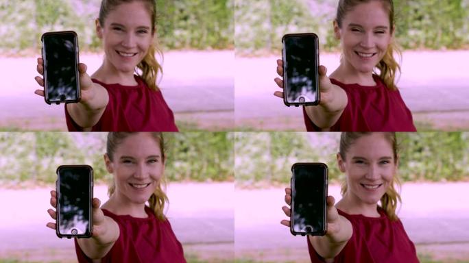 迷人的年轻女子向相机展示手机显示屏