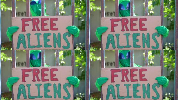 一名男子身着绿色的外星人狂欢节服装套装，在铁栅栏监狱后面的一个孤独的集会上，他的标语是 “自由的外星