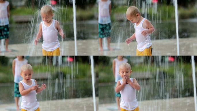可爱的蹒跚学步的男孩和哥哥，在喷气式喷泉上玩耍，到处都是水，夏天