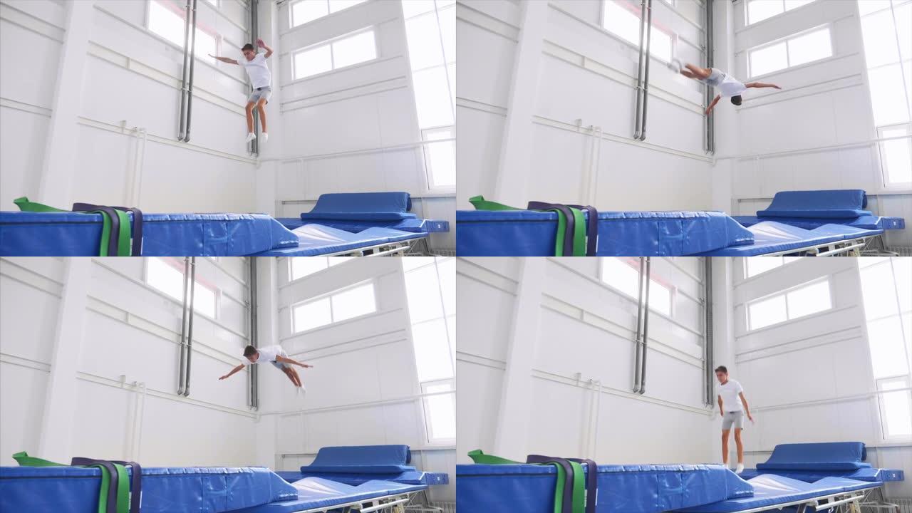 一名男孩运动员在健身房的蹦床上做后空翻，慢动作。侧视图。