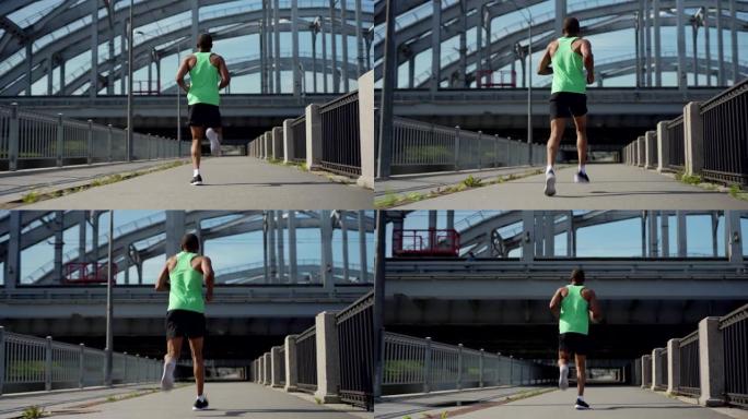 低角度后视图全程跟随镜头肌肉发达的运动员非洲人在绿色背心和运动短裤跑在桥上马拉松练习