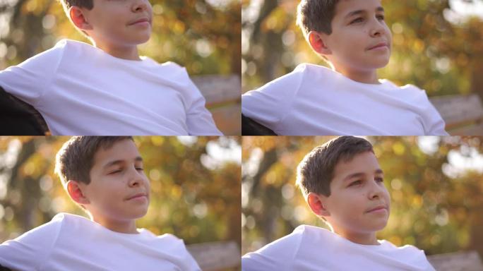 坐在长凳上的穿着白色毛衣的十几岁男孩的特写镜头。秋季公园里有背包的帅气男生