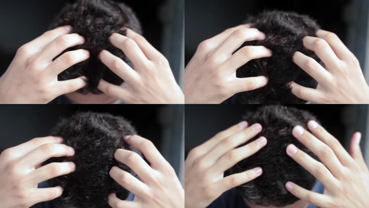 两只手在一个孤立在黑色背景上的白人男性青少年的头上做头发按摩。
