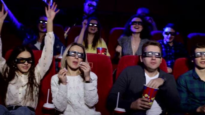 一位朋友在电影院里戴着眼镜看3D电影，他们高举双手