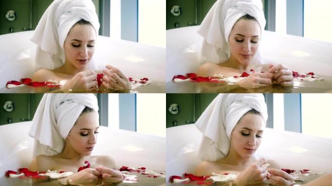 头戴浴巾的女人在浴室里用玫瑰花瓣洗澡。4 k