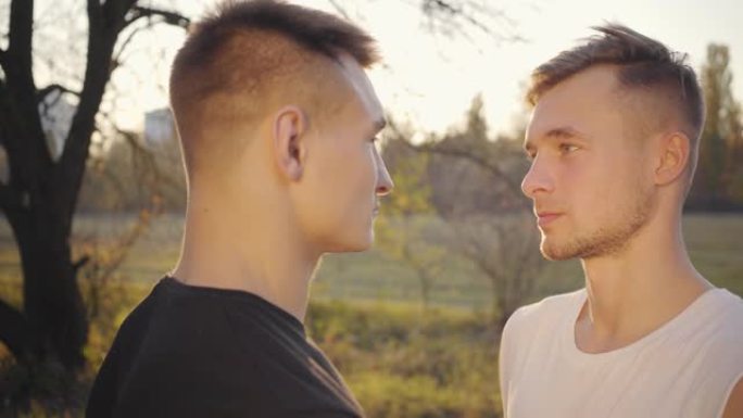 两个白人男孩在阳光下互相看着对方的特写脸。成年运动员站在户外的秋季公园。健康的生活方式，运动理念。