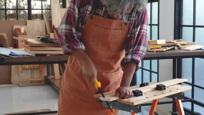 亚洲老工匠正在几个木器中锯开工作空间中的木棍