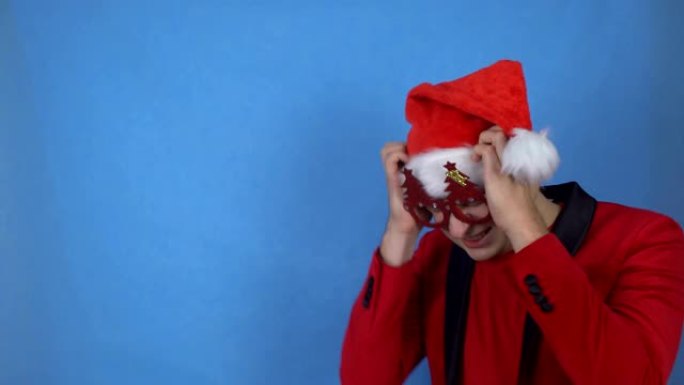 穿着圣诞老人服装的年轻人在蓝色背景上摇头，复制空间