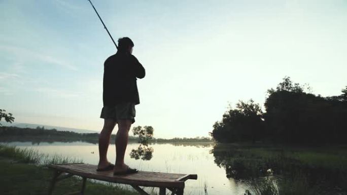 一个人独自站在湖边钓鱼时拿着钓鱼竿的剪影。