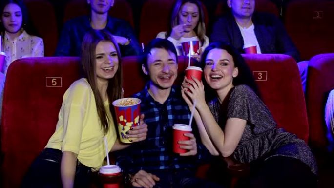 青少年坐在电影院看喜剧，吃爆米花和喝可乐