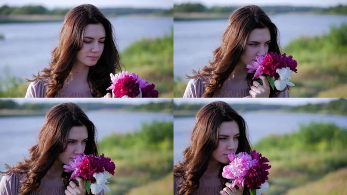 迷人的黑发女孩手里拿着一束鲜花。女孩将一束粉红色的牡丹压在胸前，嗅着花朵。