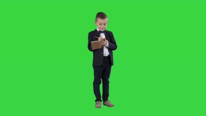 穿着正式衣服的男孩在绿色屏幕上的检查表或笔记本上写字，色键