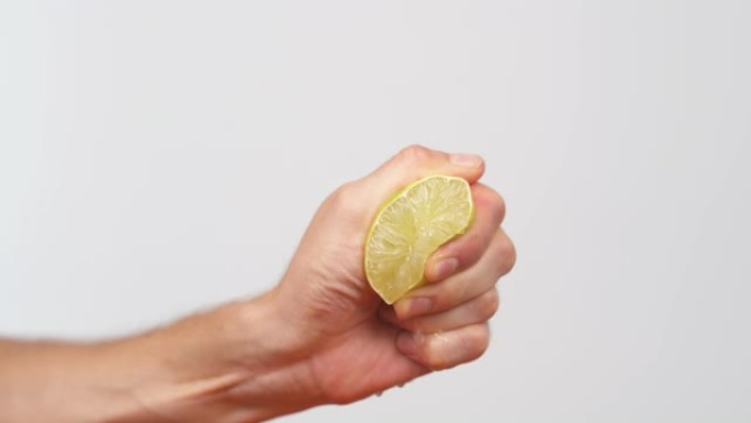 男性手握一块柠檬并将其挤出的特写镜头。柑橘汁从果肉和水滴中排出。孤立，在白色背景上