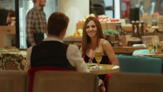 在一家昂贵的餐厅吃晚餐，一个漂亮的女孩在餐桌旁说话和微笑。一对恋人正在吃饭。肖像视图。