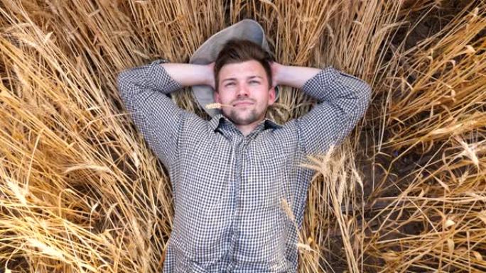 快乐的男性农民躺在大麦秸秆上，在大麦草地上放松。年轻的农艺师躺在小麦茎上，在谷物田里休息。农业商业概