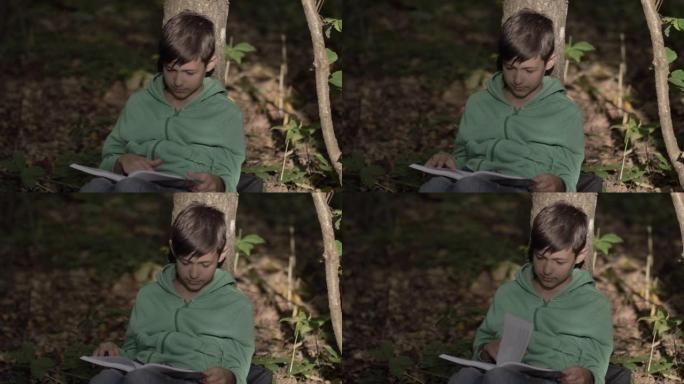 有趣的男孩坐在树下，读一本书，梦想家