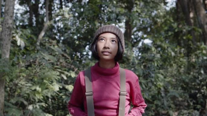 亚洲小女孩穿着长袖衬衫和羊毛帽子，一边散步，一边欣赏冬天的森林早晨的大自然。