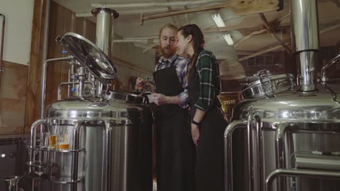 家族企业概念。男女在小型啤酒厂使用酿造机工作