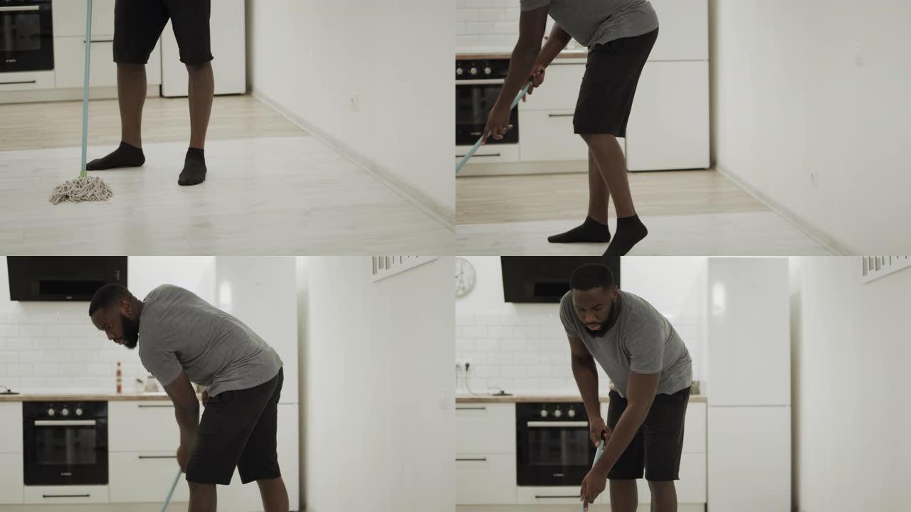 黑人在厨房用拖把清洁地板。严肃的男人穿着袜子洗地板