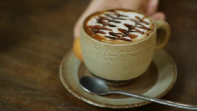 咖啡师在桌子上放了一杯拿铁咖啡。手把一杯咖啡和牛奶放在咖啡馆里。咖啡休息。特写