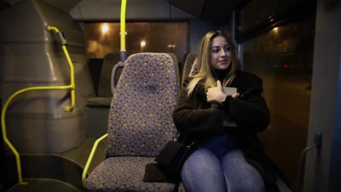 晚上乘公共汽车旅行时拿着书的女乘客。晚上，女孩在窗户旁边的行驶车辆上旅行
