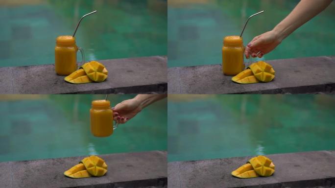 一杯芒果奶昔的特写镜头，并在游泳池的一侧切开芒果，里面装有不锈钢吸管。塑料吸管的替代品。环保产品概念