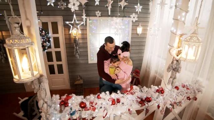 年轻的家庭与女儿在门廊拥抱并在圣诞节晚上聊天