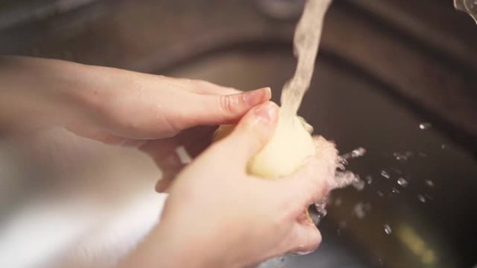 女性双手用厨房水龙头在水下洗洋葱的慢动作镜头。