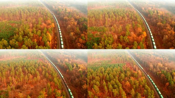 航拍镜头一列有许多货车的货运火车沿着铁路的铁轨穿越阴霾中风景如画的秋天森林。