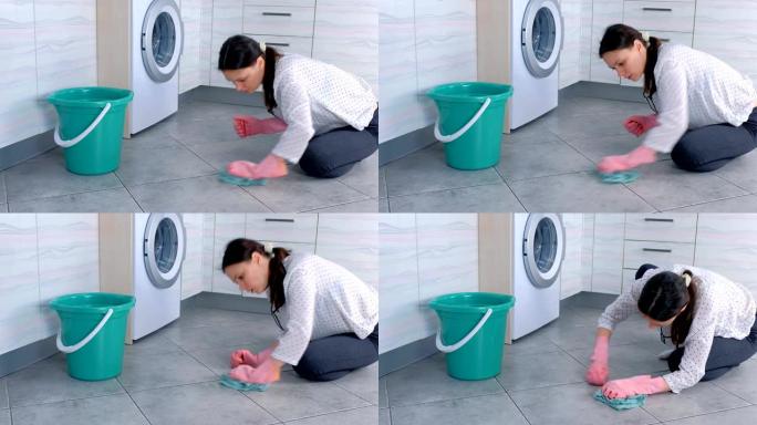穿着粉红色橡胶手套的疲倦的女人用布擦洗和擦厨房地板上的污渍。地板上的灰色瓷砖。