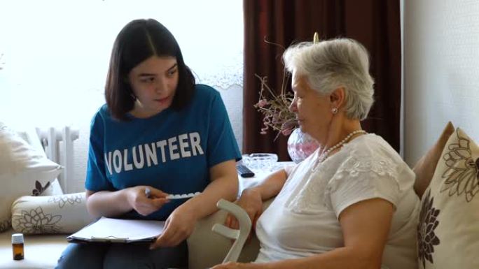 年轻的志愿者阅读处方并在家中给老年女士服药