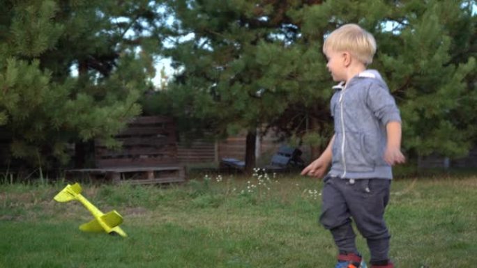 一个三岁的男孩在松树的背景下玩玩具飞机。