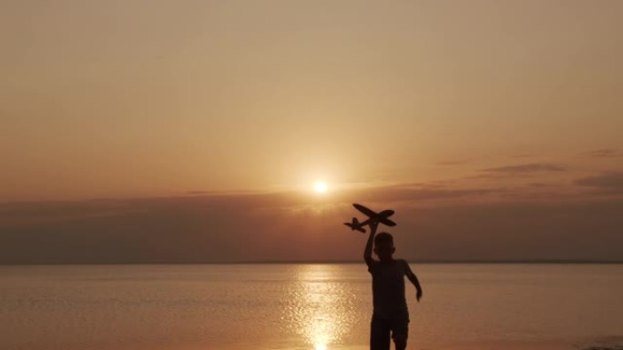 快乐的孩子在海上日落背景下与玩具飞机一起奔跑
