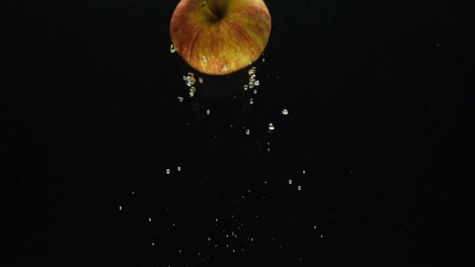 慢动作视频，一个苹果在黑色背景上掉入水中