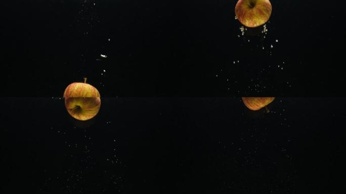 慢动作视频，一个苹果在黑色背景上掉入水中