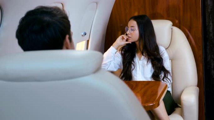戴眼镜的美丽女商人乘坐私人飞机旅行。出差。穿着经典。百万富翁女孩坐飞机坐商务舱。