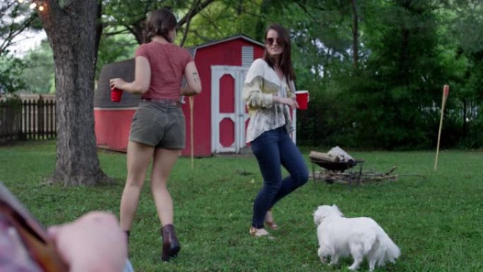 两个女人在与一只白色小狗的夏季聚会上跳舞，玩乐并大笑