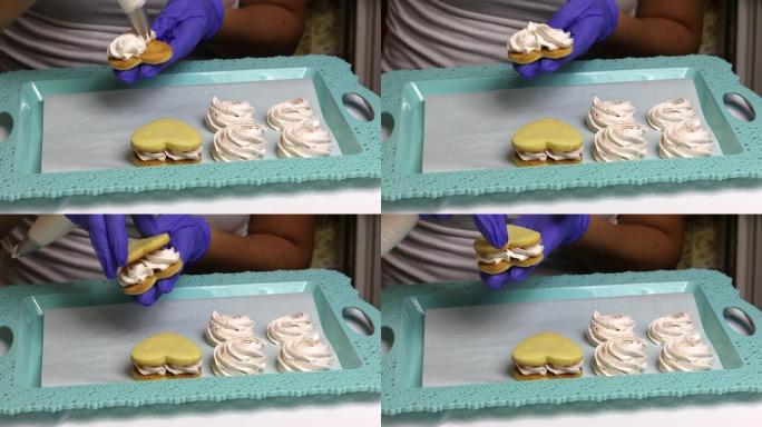 做白色棉花糖三明治的女人。将棉花糖应用于饼干饼干和托盘上。