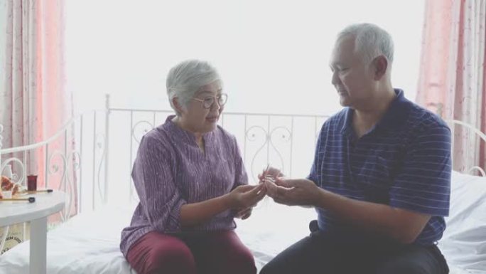 老年亚洲夫妇坐在沙发上吃老年保健药，退休夫妇吃维生素药，老年亚洲药物和保健概念