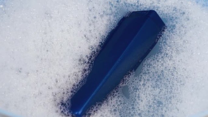 一罐蓝色的洗发水漂浮在泡沫水中。清洁和个人护理的概念。