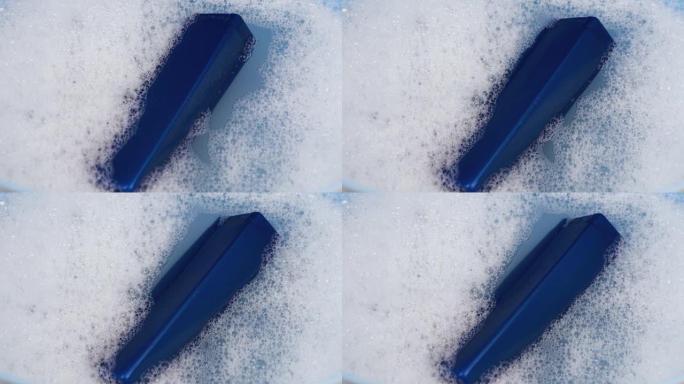 一罐蓝色的洗发水漂浮在泡沫水中。清洁和个人护理的概念。