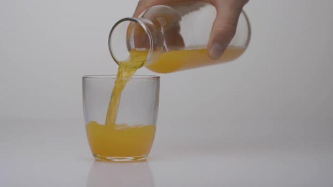 甜的含糖橙色饮料从锅里倒入玻璃杯中。高热量饮料。不健康的食物概念